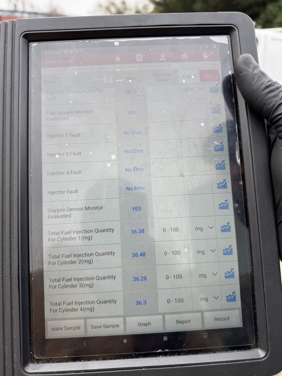 A gloved hand holding a diagnostic tablet showing live engine readings